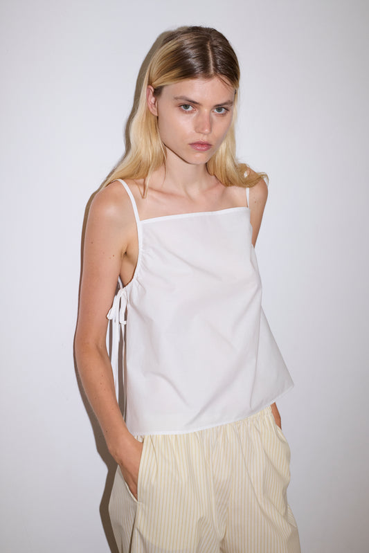 blonde female model wears a white lightweight top featuring fixed gathered armholes and right hand side armhole keyhole and ties, paired with a butter yellow striped ankle length pant features a soft minimal elastic waist with side seam pockets in a straight leg