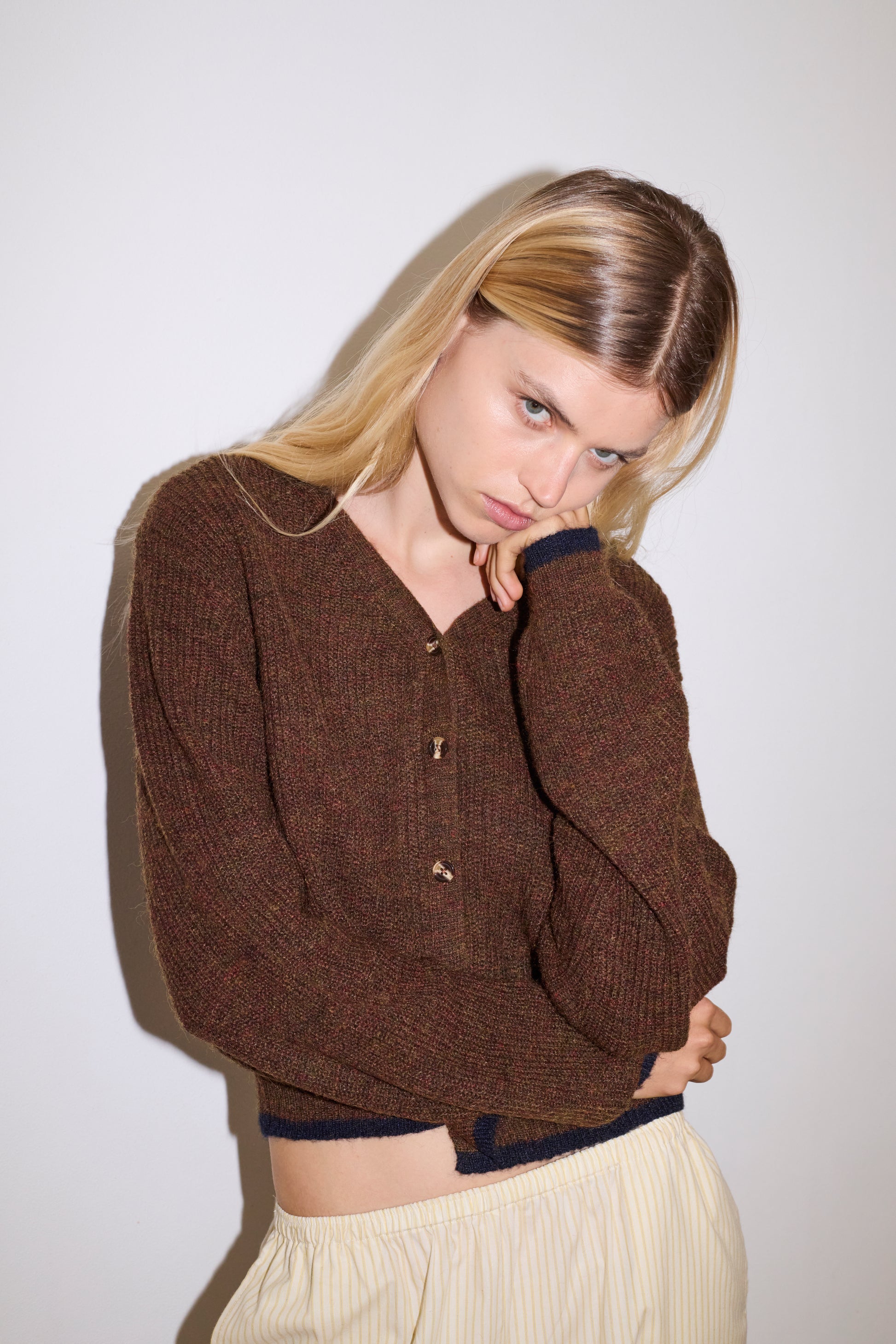 blonde female model wears long sleeve cardigan in brown merino wool fabric with navy stripe hem detail and button down front, worn with an elasticated waist yellow striped full-length trouser