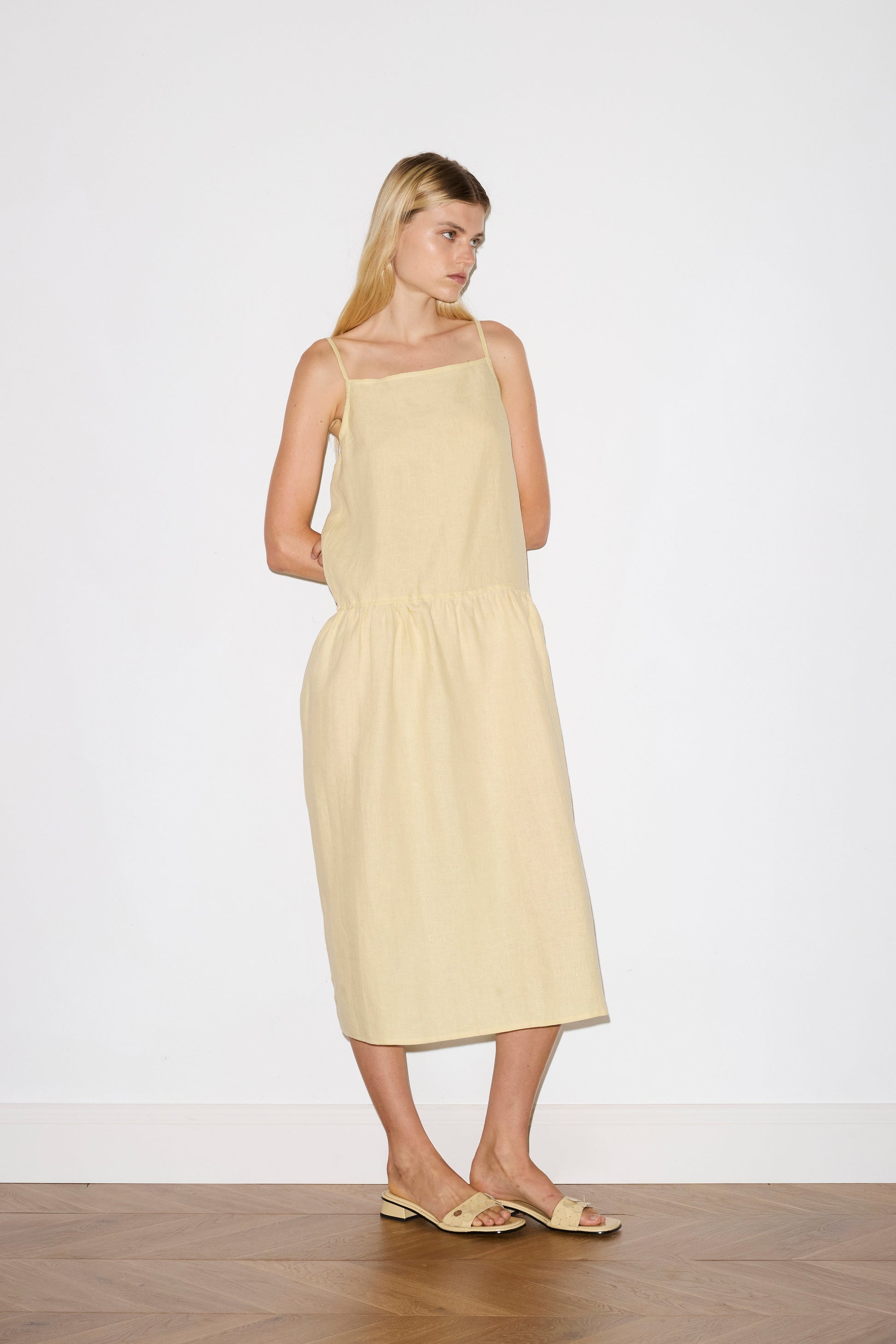 blonde haired female model wears a butter yellow relaxed mid-length dress featuring a drop waist with soft gathered skirt, gathering under the armholes and adjustable tie straps at back