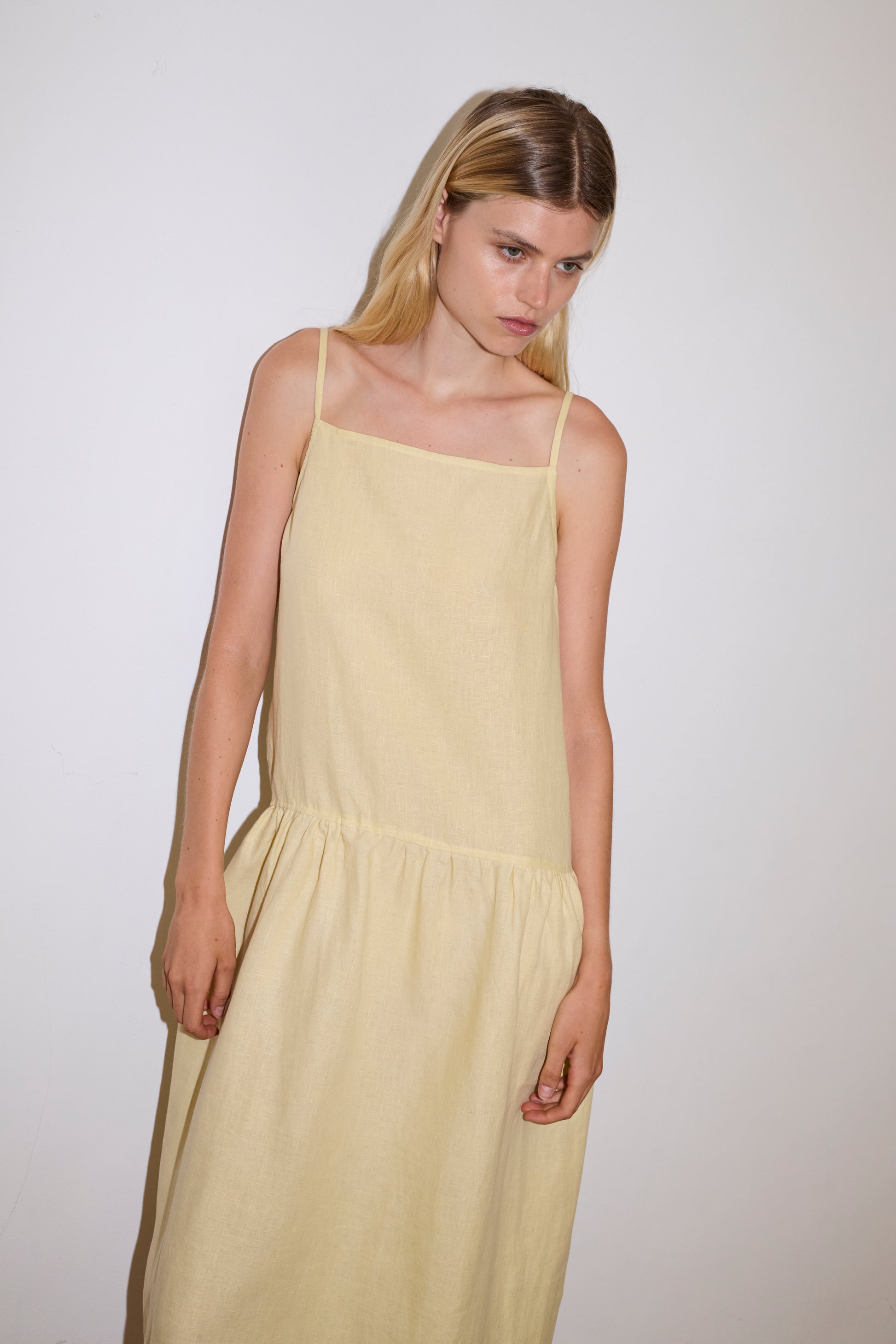 blonde haired female model wears a butter yellow relaxed mid-length dress featuring a drop waist with soft gathered skirt, gathering under the armholes and adjustable tie straps at back