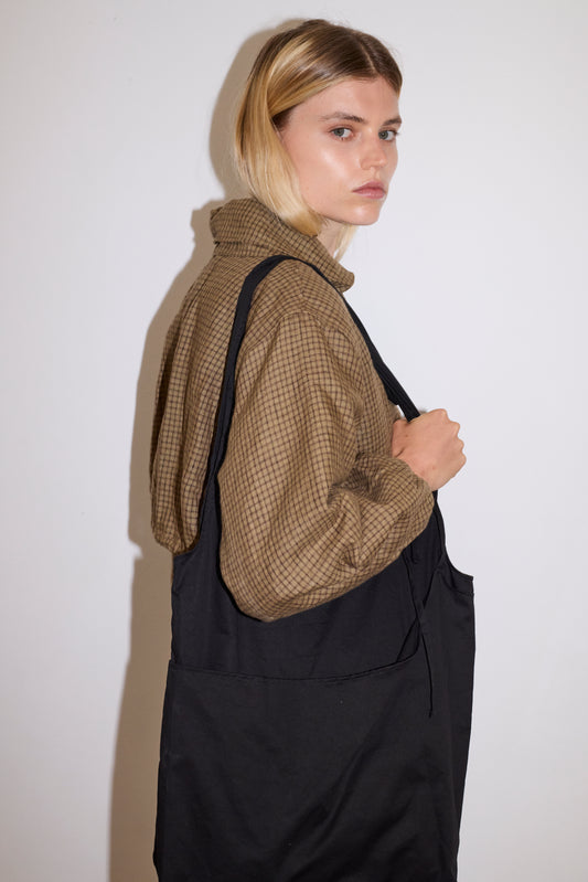 blonde female model wears a black elevated, medium weight double layered tote featuring fixed shoulder straps with a tie detail and flat base paired with a black and brown gingham print zip up cotton jacket 