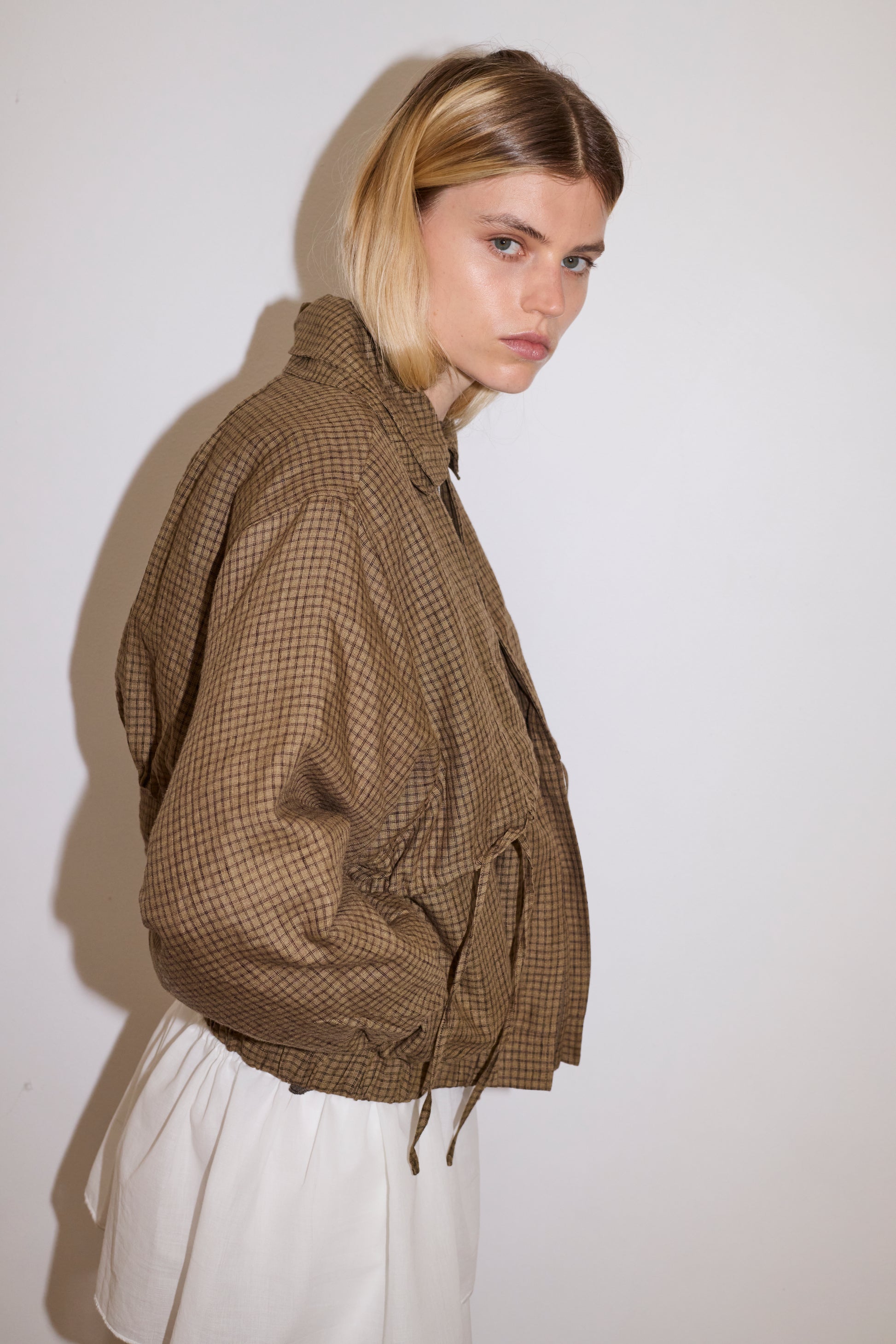 female model wears organic cotton jacket in brown and black checkered pattern, worn white trouser