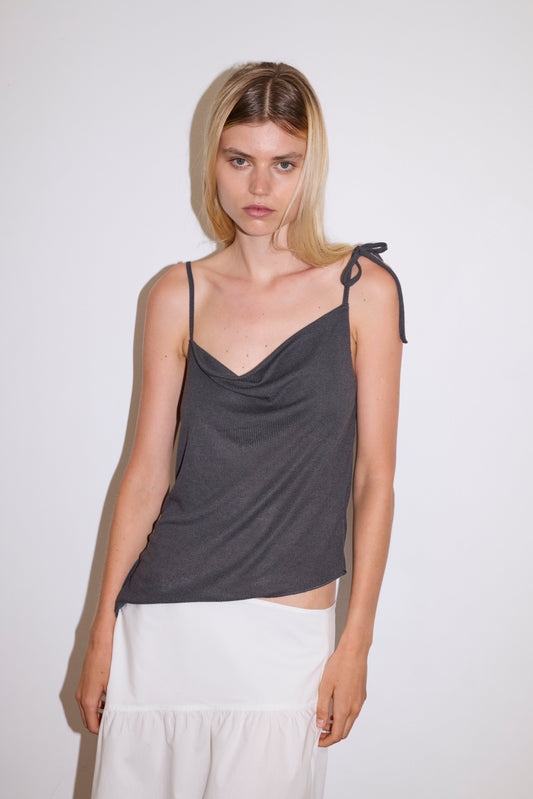 blonde female model wears a sheer fine knit relaxed tank with a fold over cowl neckline and low draping back, features self fabric rouleau straps, baby lock hem finishes and a asymmetric bottom detail, worn with a midi length white skirt 