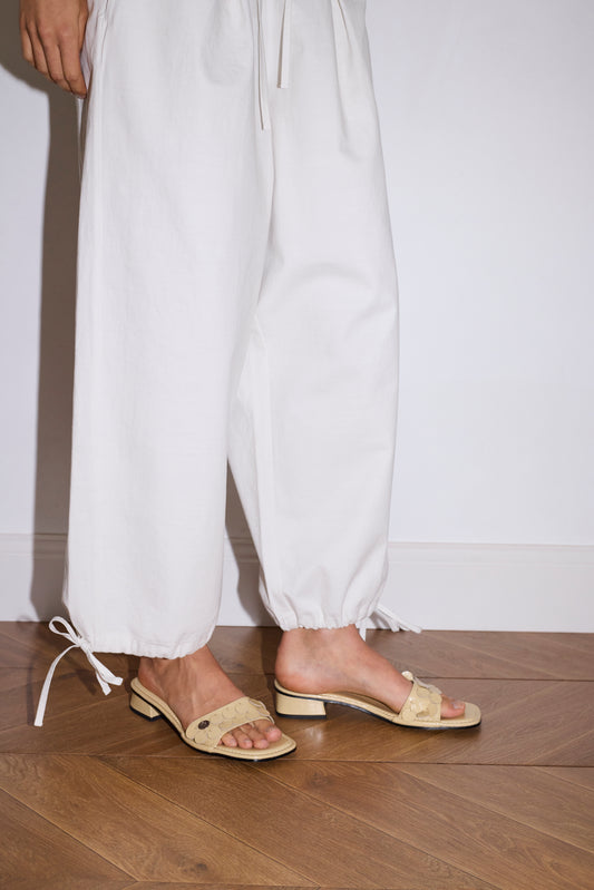 Wearing Deiji Studios' Drawcord Wide Leg Pant in white and beige sandals, a person stands on a wooden floor against a plain white wall.