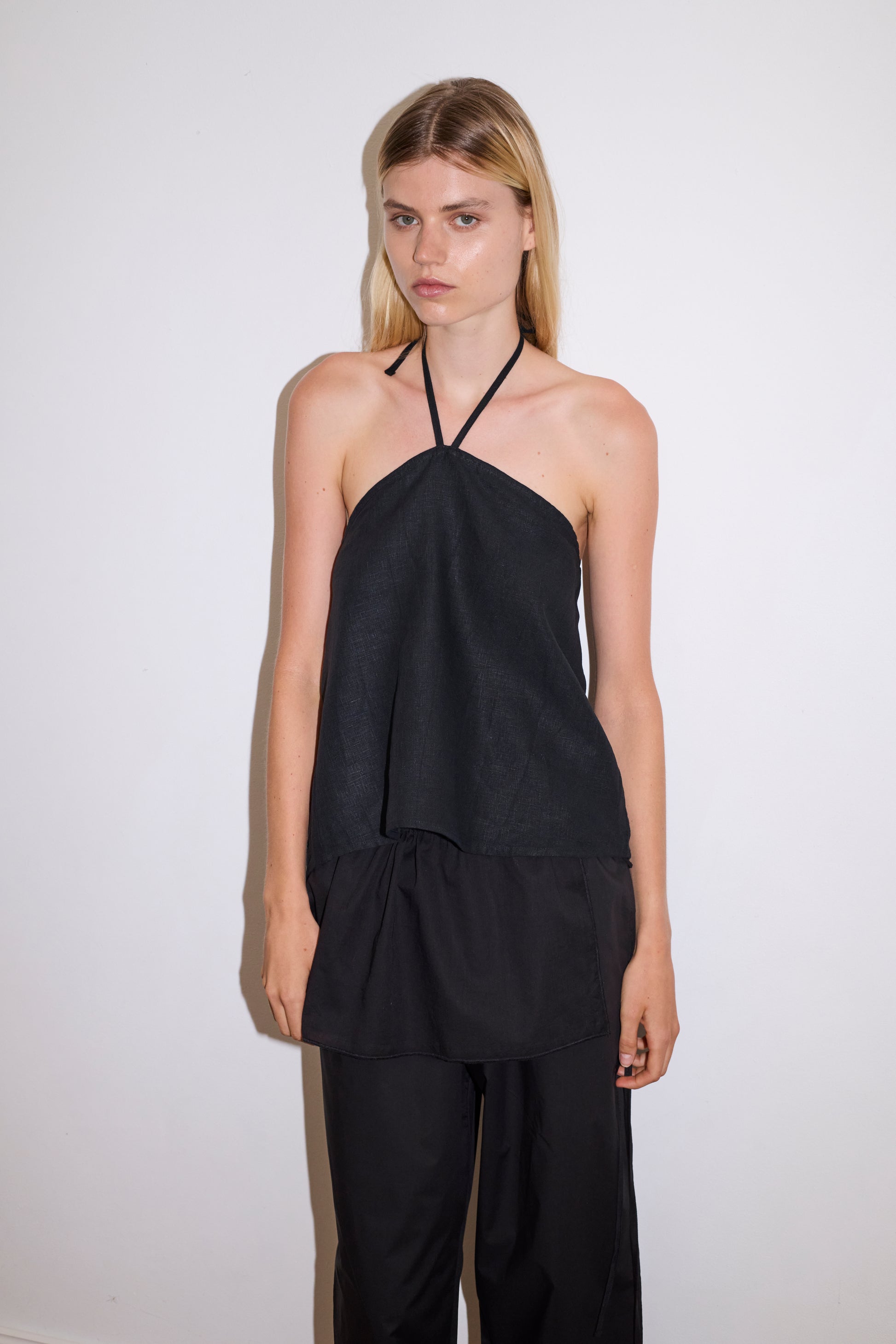 blonde female model wears a black lightweight wrap belt features a drawcord casing, adjustable ties to wrap the body, and a babylock hem, paired with a black cotton trouser and black linen wrap top