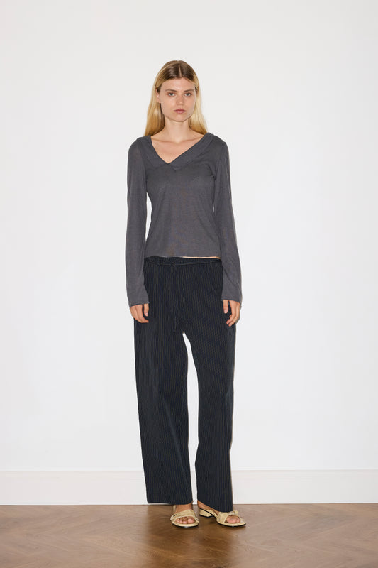 blonde female model wears grey long sleeve top, worn with a navy and yellow striped trouser 