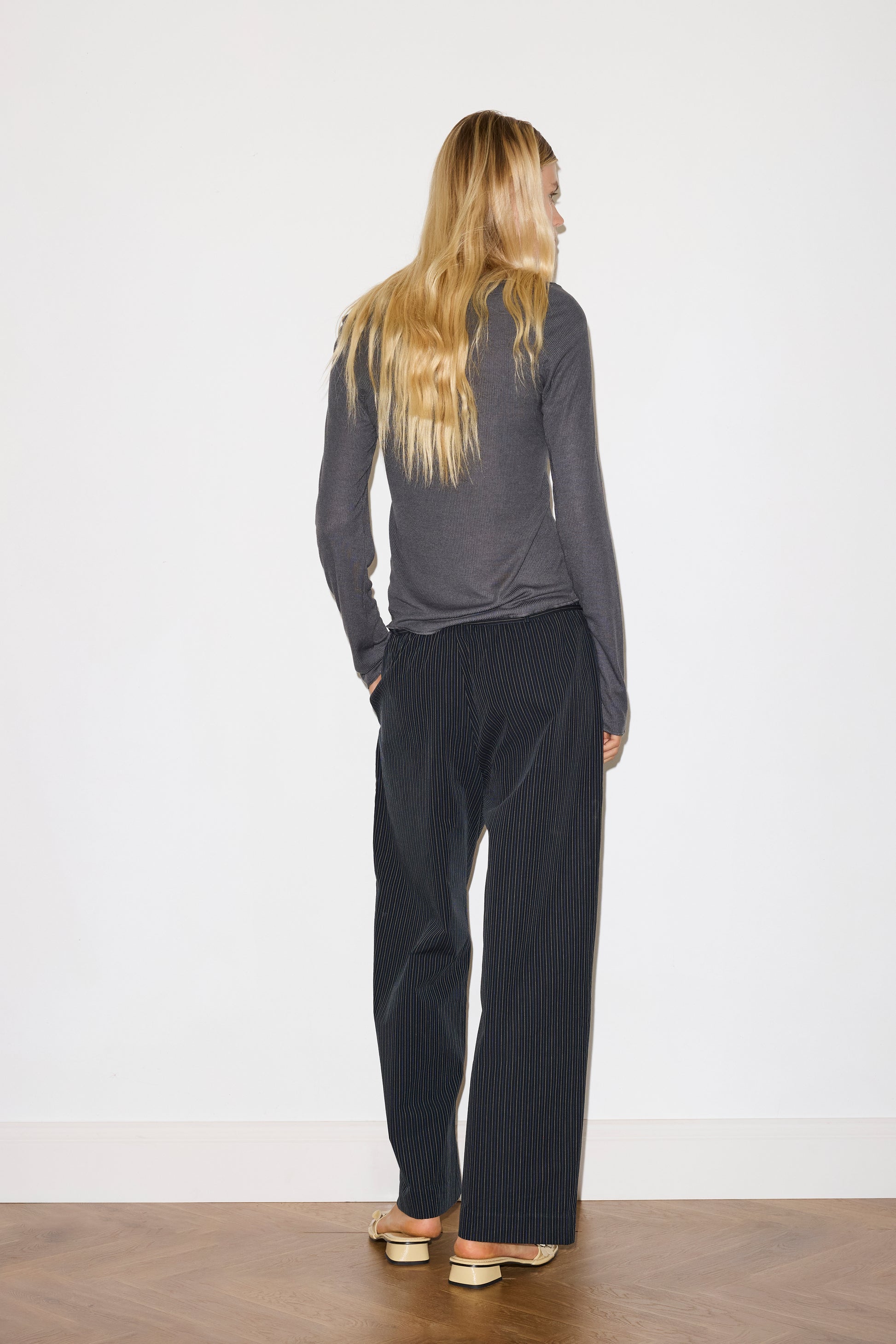 blonde female model wears grey long sleeve top, worn with a navy and yellow striped trouser 