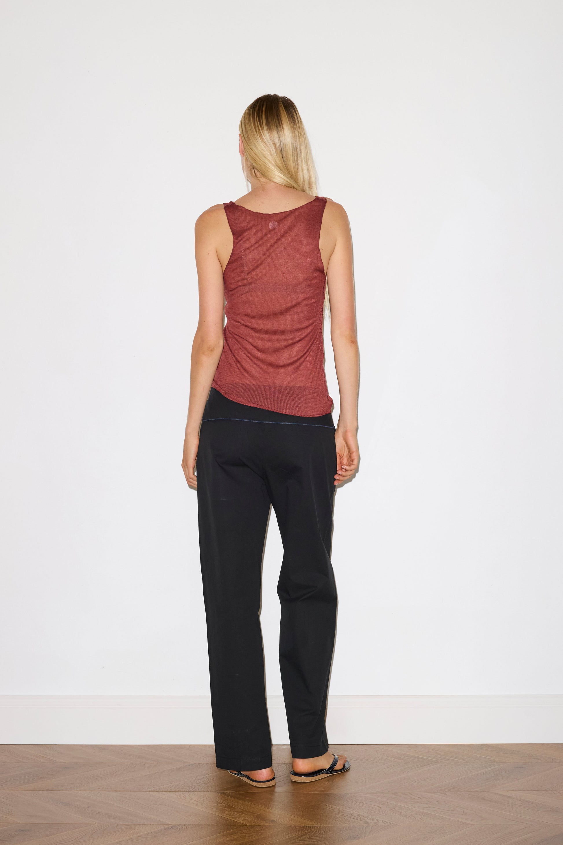 blonde female model wears a knit tank in crimson red in a sheer material, worn with a full-length black trouser with tie belt detail and size zip closure.