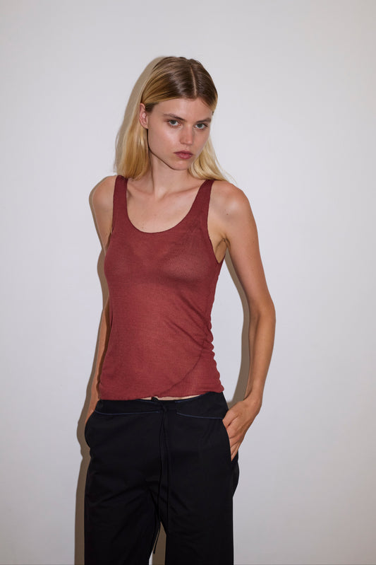 blonde female model wears a knit tank in crimson red in a sheer material, worn with a full-length black trouser with tie belt detail and size zip closure.