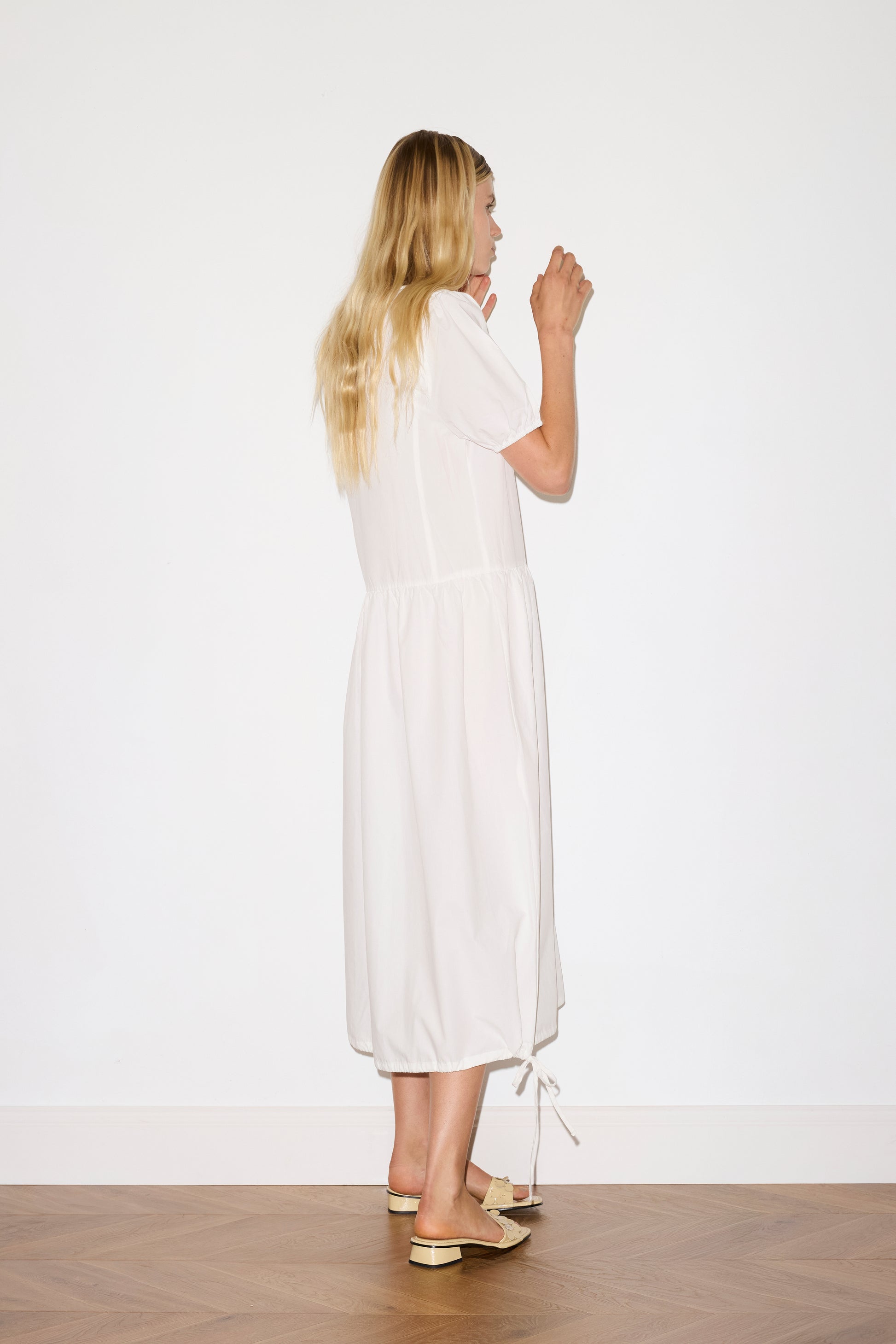 blonde female model wears a white elevated everyday dress in mid length features a flattering v neckline with tie, button front detail with a drop waist, and soft elastic blouson sleeve