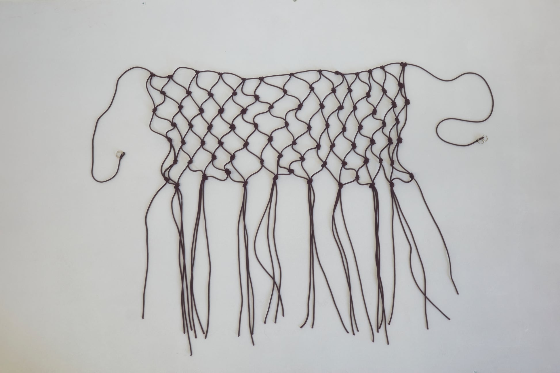 A handwoven black macramé belt made from recycled polyester, featuring loose ends and fringes, displayed flat on a white background.