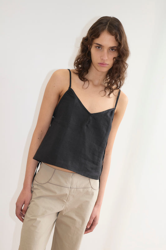 A person with wavy brown hair wears the Deiji Studios V Neck Cami in black and beige pants, standing against a plain white background while looking at the camera with a neutral expression.