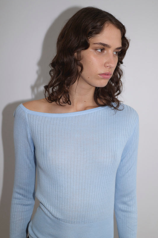 A person with wavy brown hair wears the Shoulder Knit Top - Blue from Deiji Studios, standing against a plain white background and looking slightly to the side with a neutral expression.