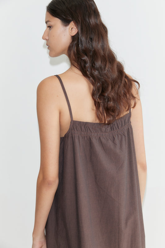 A woman with long, wavy brown hair faces away, wearing the Light Maxi Dress - Toast with thin straps, set against a plain white background.