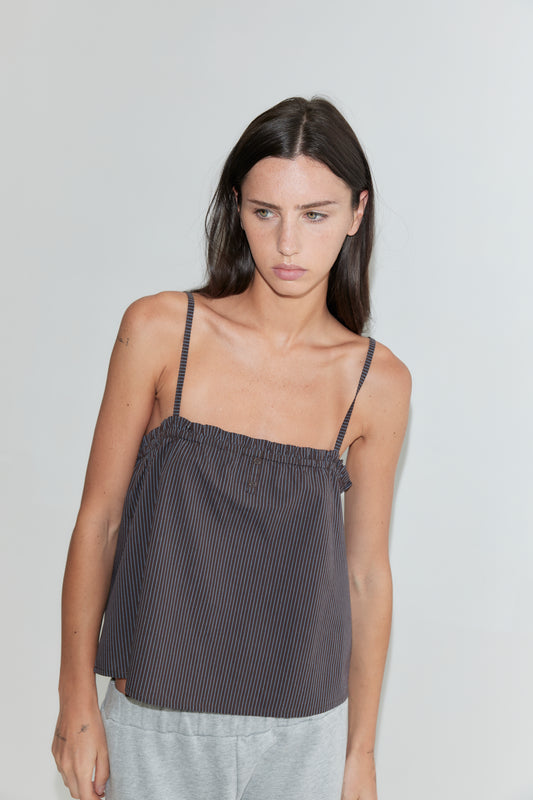 A cropped front view of the Frill Placket Top - Brown Blue Stripe by Deiji Studios, a dark brown fine-striped cami top with thin straps and a gathered frill placket, worn with grey marle trousers against a plain white background.
