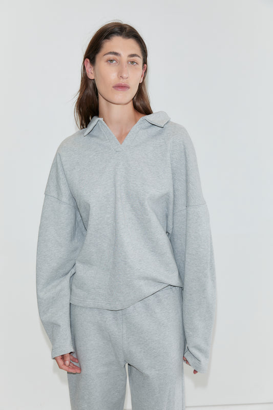 A person with long brown hair wearing the Jersey Jumper in Grey Marle stands against a plain white background, looking at the camera with a neutral expression.