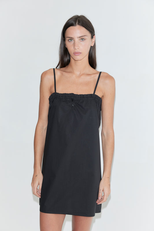 A cropped front view of the Frill Placket Dress - Black by Deiji Studios, a black mini dress with thin straps and a gathered, buttoned frill placket at the neckline, against a plain white background.