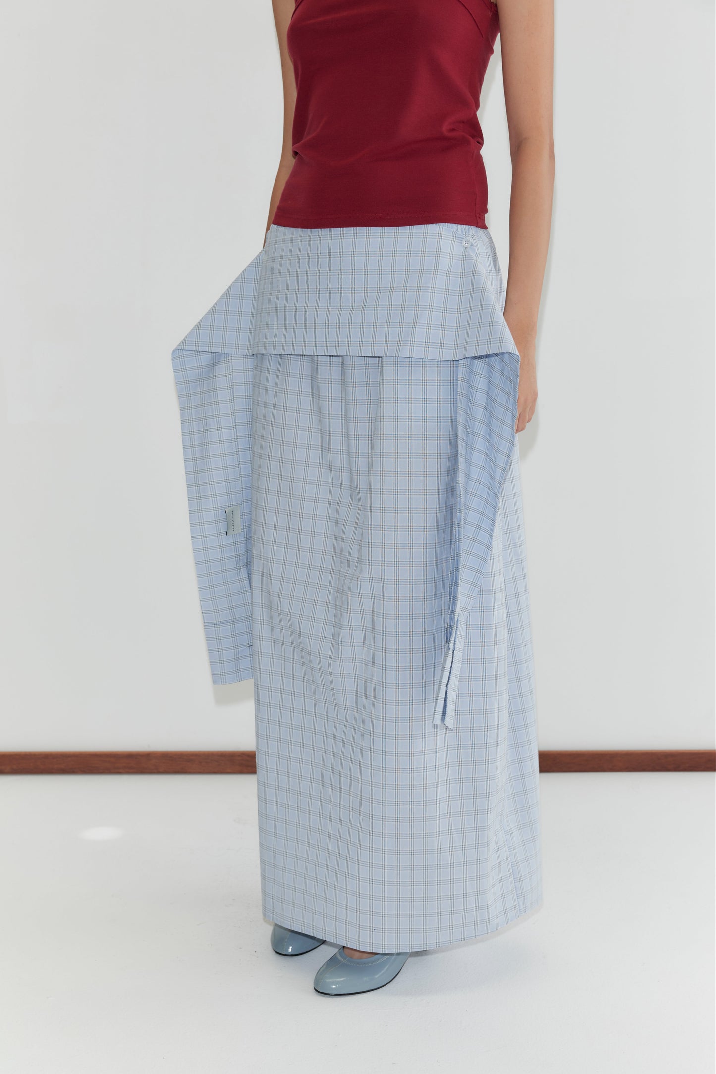 A person wears a red sleeveless top and a long, light blue plaid skirt featuring the Shirt Cuff Belt - Powder Check at the waist, standing against a white background in deiji studios style.