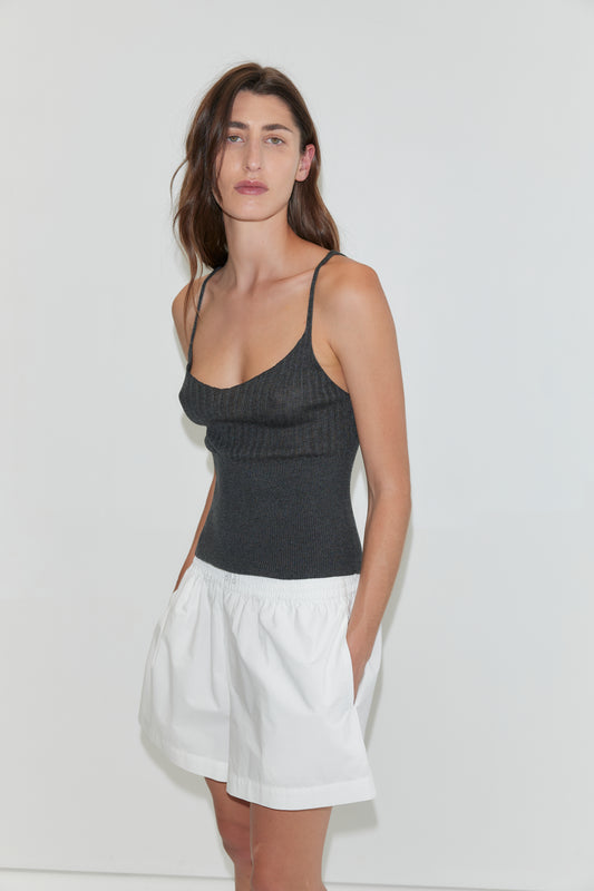 A woman with long brown hair wears a dark tank top and Deiji Studios' Organic Cotton Boxer - White. She stands against a plain white background with her hands in her pockets, gazing neutrally at the camera.