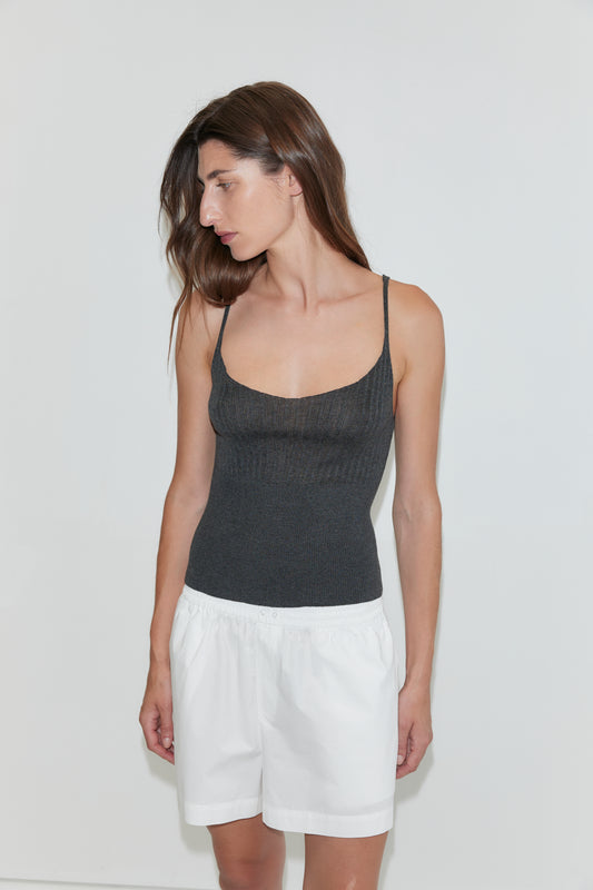 A woman with long brown hair wears a fitted, dark gray tank top and loose white Organic Cotton Boxer - White shorts, standing against a plain white background and looking to her left.