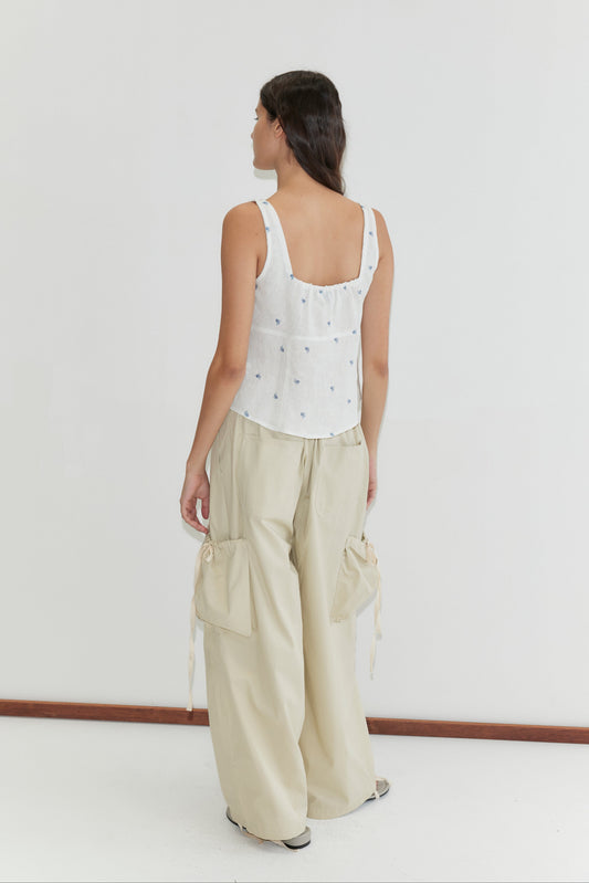 A woman with long dark hair stands facing away, wearing the Relax Tie Top - Floral Blue by Deiji Studios and loose light beige cargo pants. She is set against a plain white background.