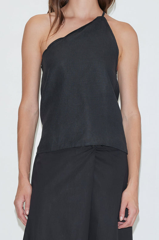 A woman stands against a plain white background wearing the Deiji Studios Half Halter - Black, a sleeveless, one-shoulder linen top, paired with a matching black skirt.