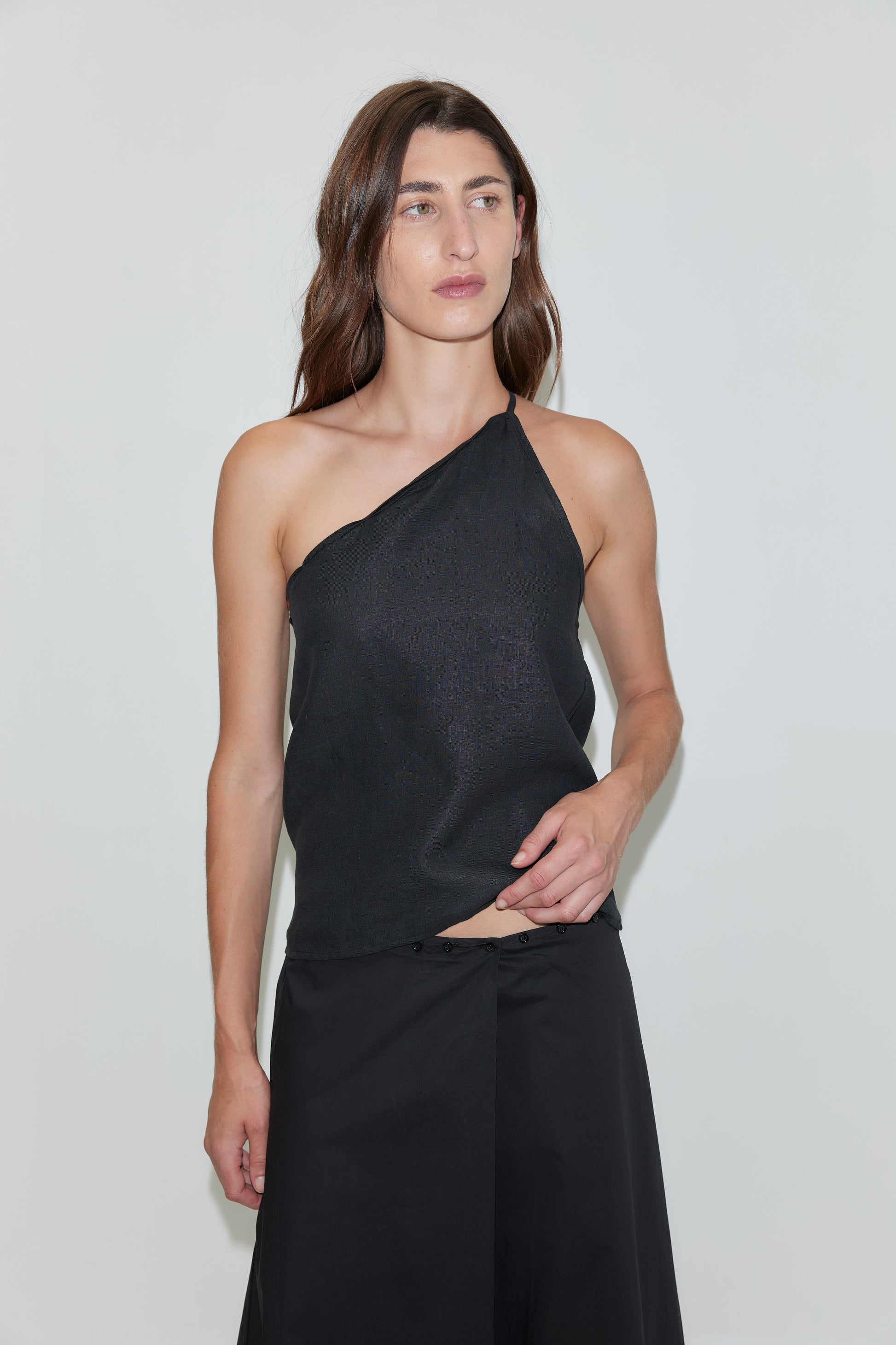 A person with long brown hair wears the Half Halter - Black from Deiji Studios and black pants, standing against a plain white background.