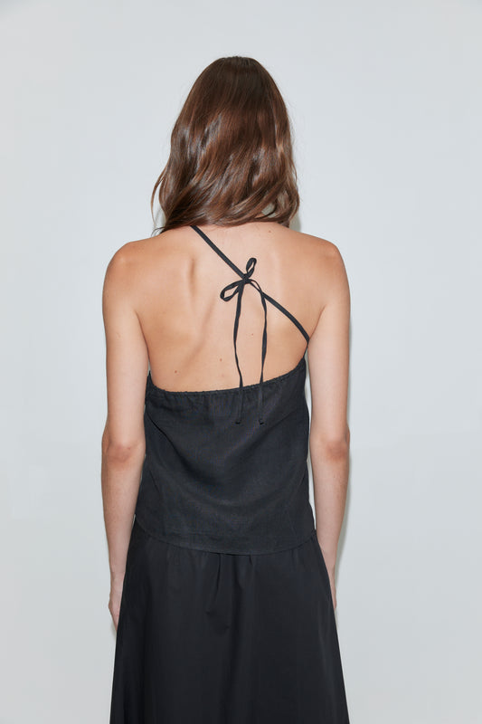 Woman with long brown hair wearing the Half Halter - Black, paired with a black skirt and seen from the back against a plain light background—a look that effortlessly captures the minimalist elegance often found in Deiji Studios collections.