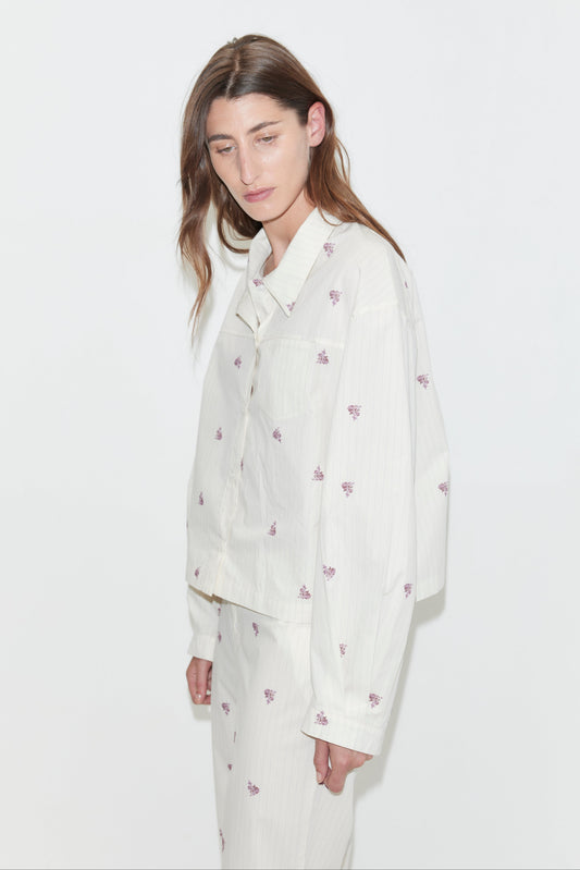 A person with long brown hair wears the oversized cotton poplin Boxy Long Set - Floral Stripe, which features a subtle purple floral pattern, standing against a plain white background.