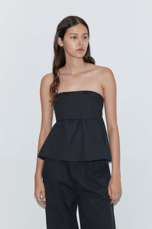 A woman with long brown hair wears the Flow Top - Mono Grid by Deiji Studios, styled with loose black pants and standing against a plain light background.