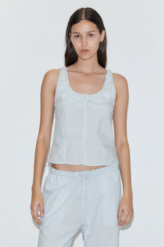 A woman with long dark hair wears the Deiji Studios Frills Top - Mist Stripe, a light blue and white striped cotton poplin tank, paired with matching pants, standing against a plain white background.
