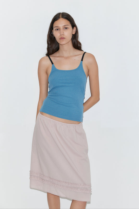 A woman with long brown hair wears the Daytime Skirt - Floss and a blue tank top with black straps, standing against a plain white background and looking at the camera with a neutral expression.