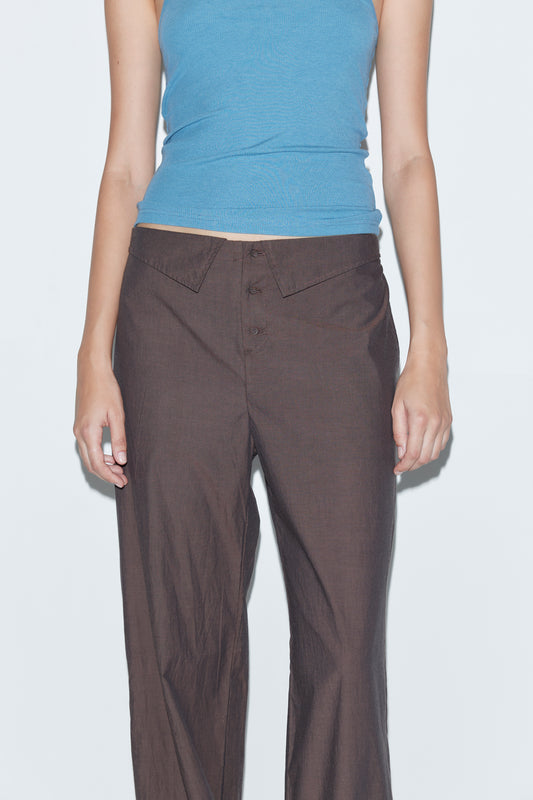 A person wears a light blue sleeveless top and the Collar Point Pant - Toast by Deiji Studios, standing against a plain light background and shown from shoulders to mid-thigh.
