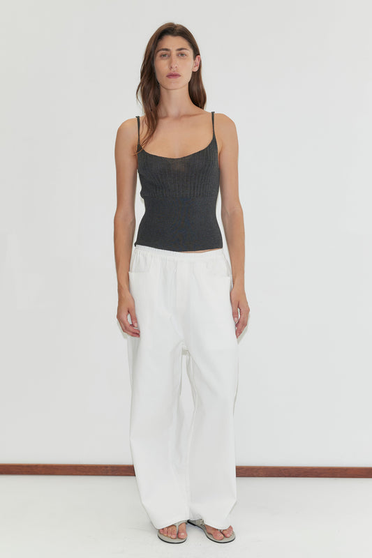 A woman with long brown hair, a neutral expression, and arms at her sides stands against a plain white background wearing the Square Pocket Pant in White and a dark gray sleeveless knit top.