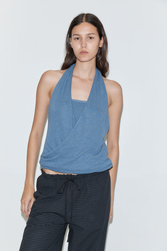 A woman with long dark hair wears the Double Layer Jersey Halter - Blue from Deiji Studios and black drawstring pants, standing against a plain white background with a neutral expression.