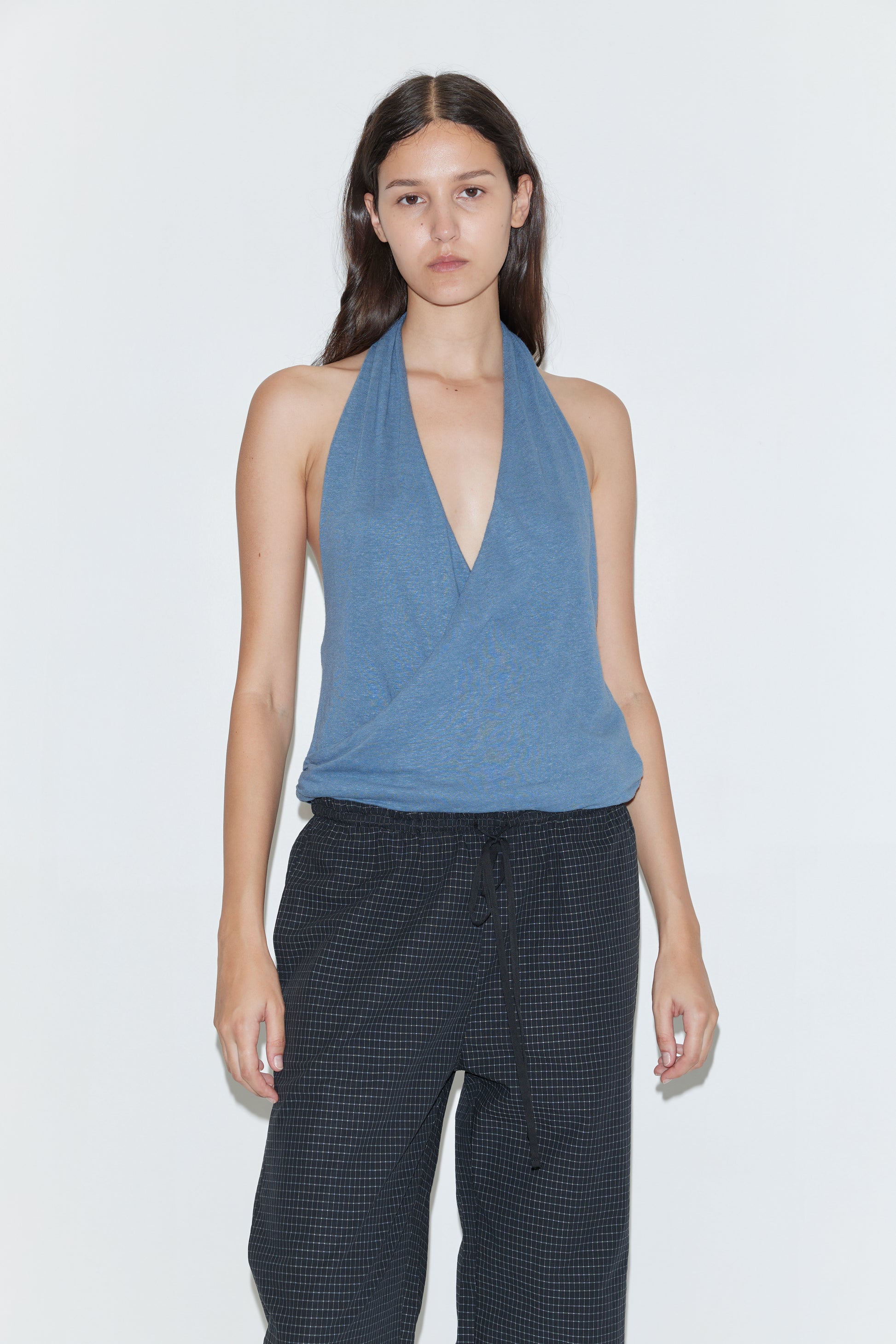 A woman with long brown hair wears the Double Layer Jersey Halter - Blue and loose black pants, standing against a plain white background with a neutral expression.