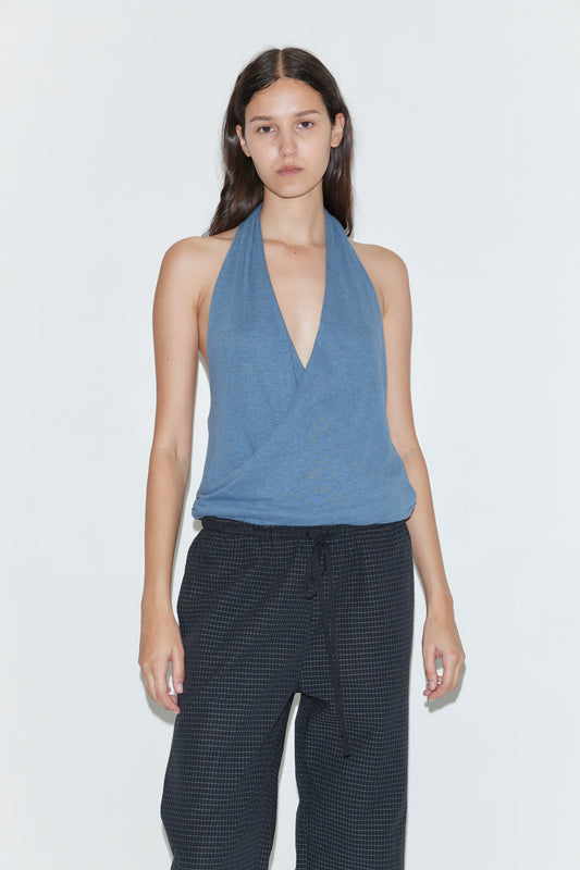 A woman with long brown hair wears the Double Layer Jersey Halter - Blue and loose black pants, standing against a plain white background with a neutral expression.