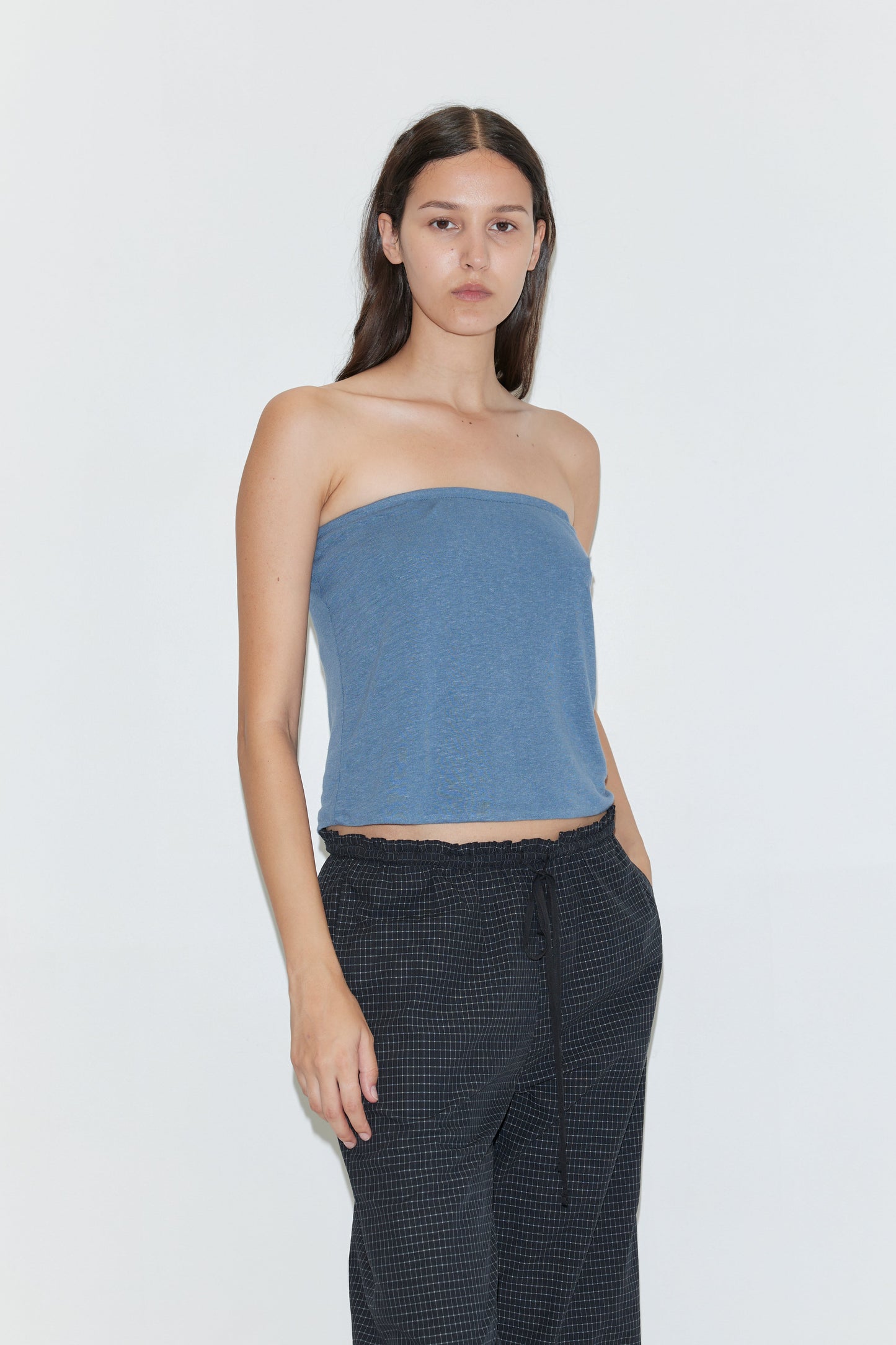 A woman with long brown hair models the Double Layer Jersey Halter - Blue, paired with dark drawstring pants, standing against a plain white background and looking directly at the camera.