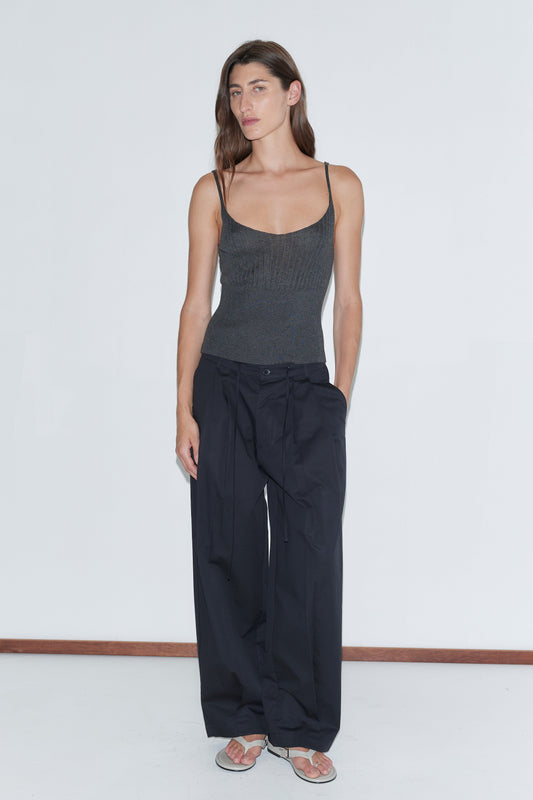 A woman wearing the Turn Pant - Black from Deiji Studios stands in front of a white wall, embodying effortless style in soft organic cotton.