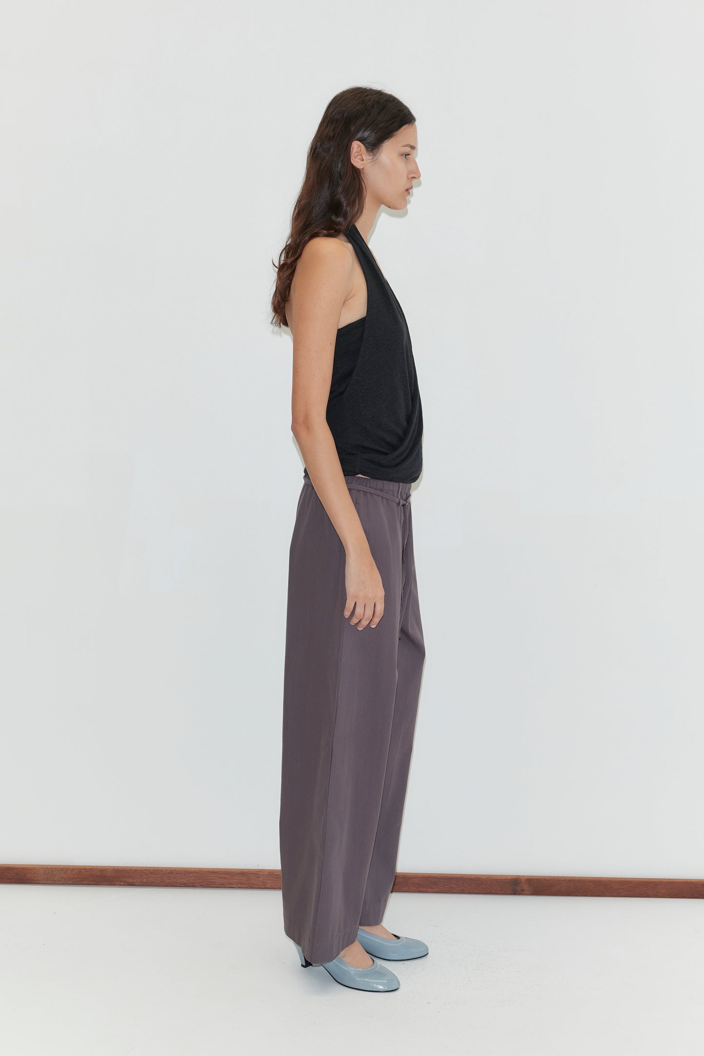 A woman with long brown hair stands in profile against a white background, wearing a sleeveless black top and the Loop Pant - Mulberry Stripe.