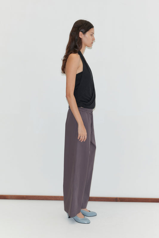 A woman with long brown hair stands in profile against a white background, wearing a sleeveless black top and the Loop Pant - Mulberry Stripe.