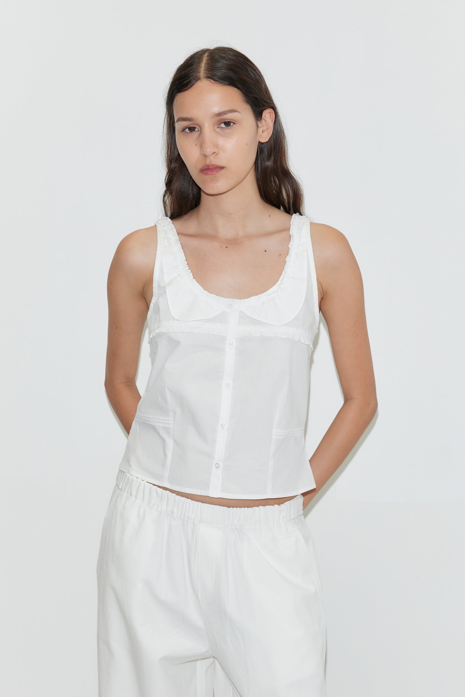 A woman with long brown hair, wearing the Frills Top - White and loose-fitting white pants, stands against a plain white background.