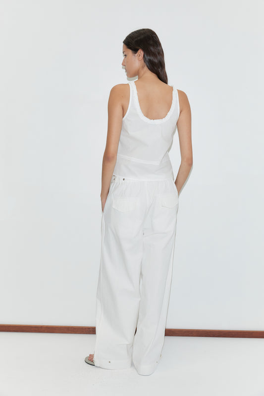 A woman with long dark hair, facing away, wears a sleeveless white top and Snap Tab Pant - White by Deiji Studios featuring wide legs and back pockets, posed against a plain white background.