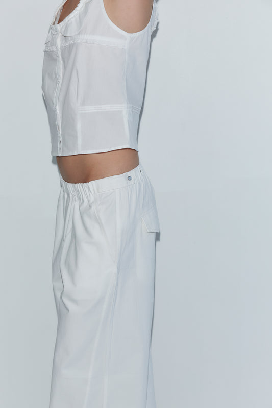 A person in profile, face not visible, wears a sleeveless white blouse and the Snap Tab Pant - White from Deiji Studios against a plain light background.