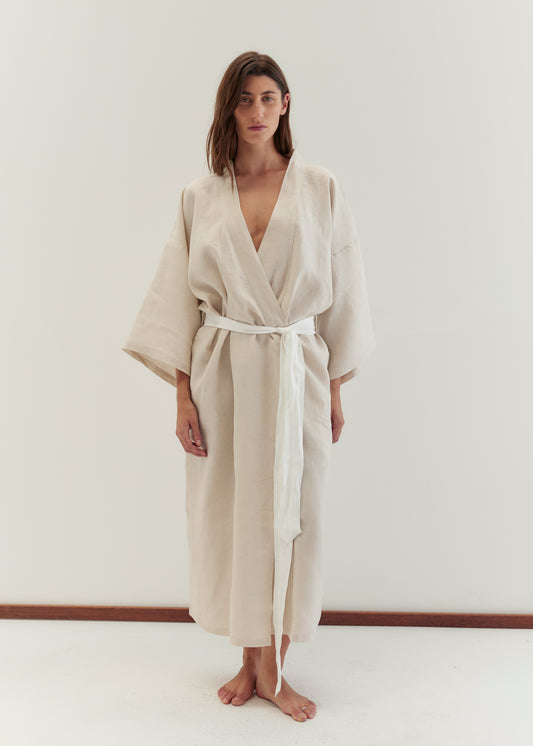 A woman stands barefoot against a white background, wearing the 02 robe in oatmeal—a loose-fitting style with wide sleeves and a linen waist tie—as she looks directly at the camera with a neutral expression.