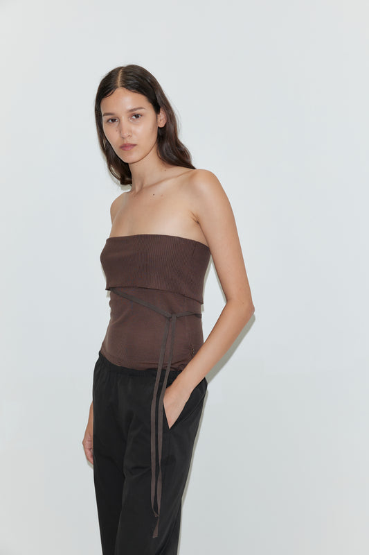 A woman with long dark hair wears the Capri Pant in Black by Deiji Studios, paired with a strapless brown top, standing against a plain white background.