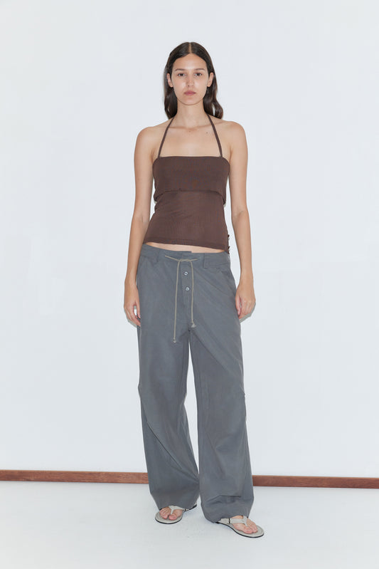 A person stands against a white background wearing a brown strapless top, flip-flops, and the Deiji Studios Panel Leg Pant in Charcoal, which features a relaxed fit and drawstring waist. They have long, straight hair and a neutral expression.