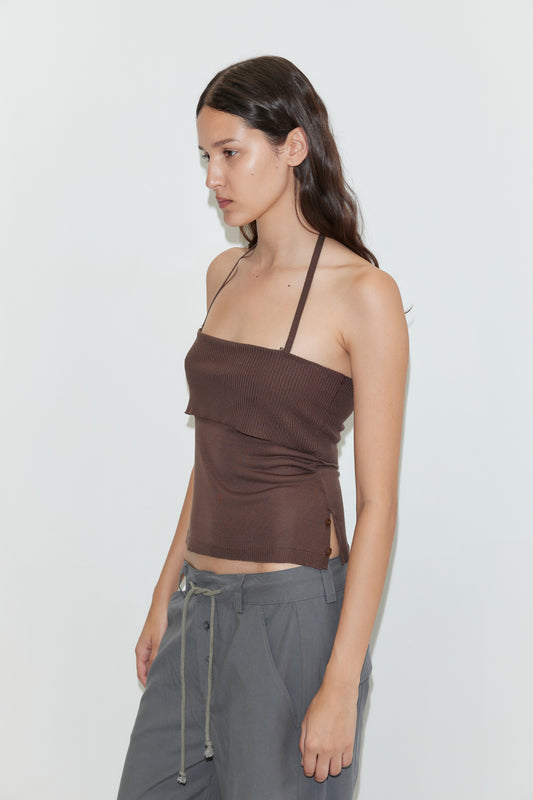 A woman with long brown hair, wearing a brown halter top and Deiji Studios Panel Leg Pant in Charcoal, stands against a plain white background facing left in a relaxed pose.