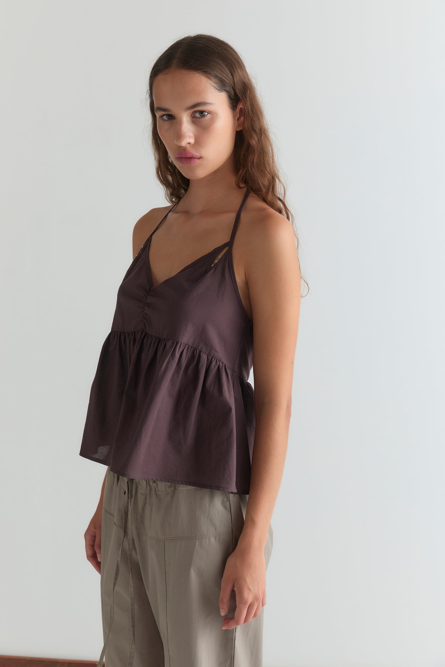 A woman with long brown hair wears the Keyhole Halter Top - Wine and light beige pants, standing against a plain light background and looking toward the camera with a neutral expression.