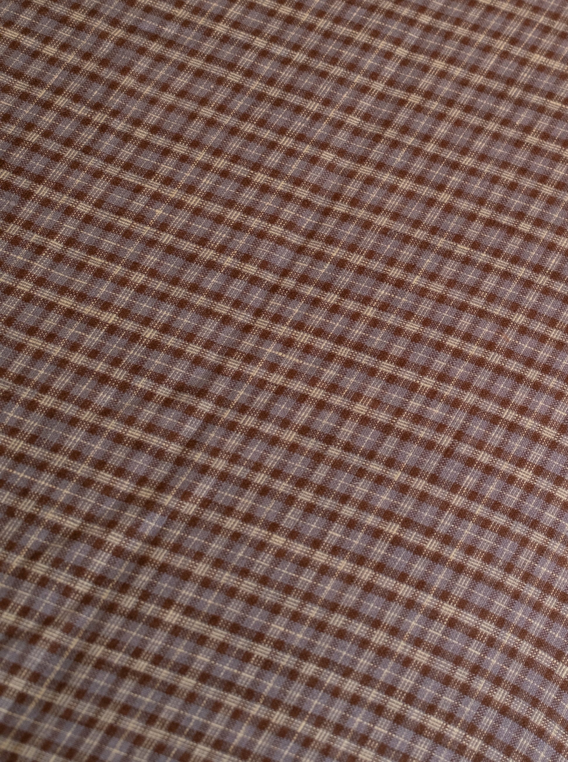 Close-up of the russet check linen ease trouser from Deiji Studios, featuring brown and beige plaid French linen in a diagonal square pattern—texture and weave shown, reflecting the effortless style of these trousers.